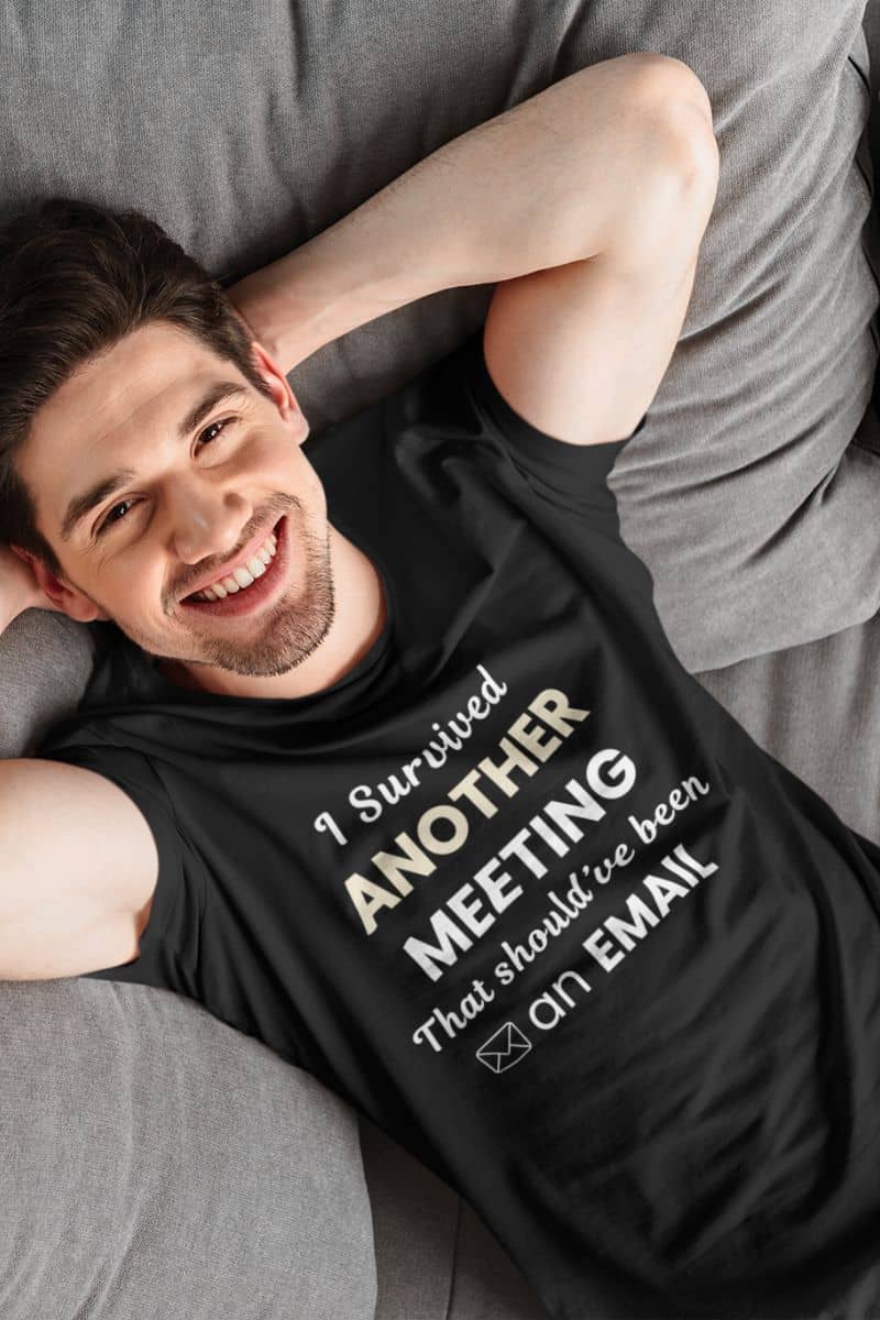 office humor shirt with a man wearing a black t-shirt with text 'I Survived Another Meeting That Should’ve Been an Email', lying on a couch.
