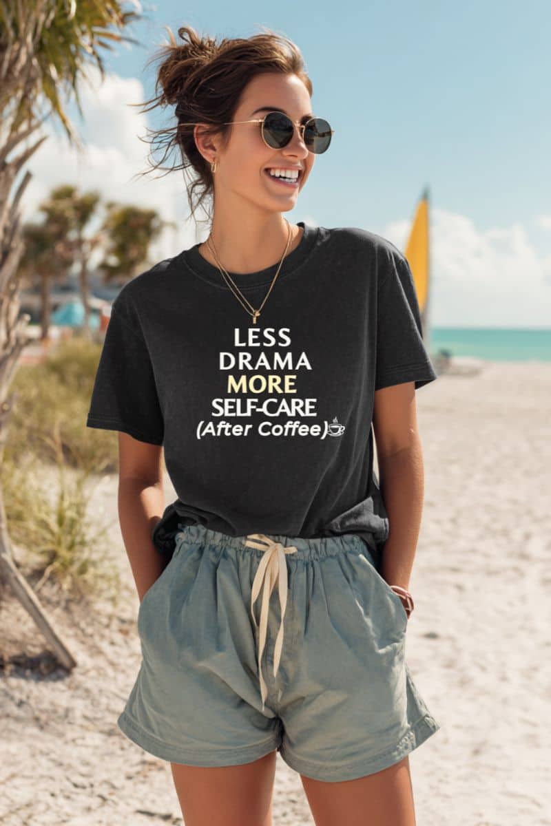 office humor shirt with a woman wearing a black t-shirt with text 'Less Drama, More Self-Care (After Coffee)' on a beach