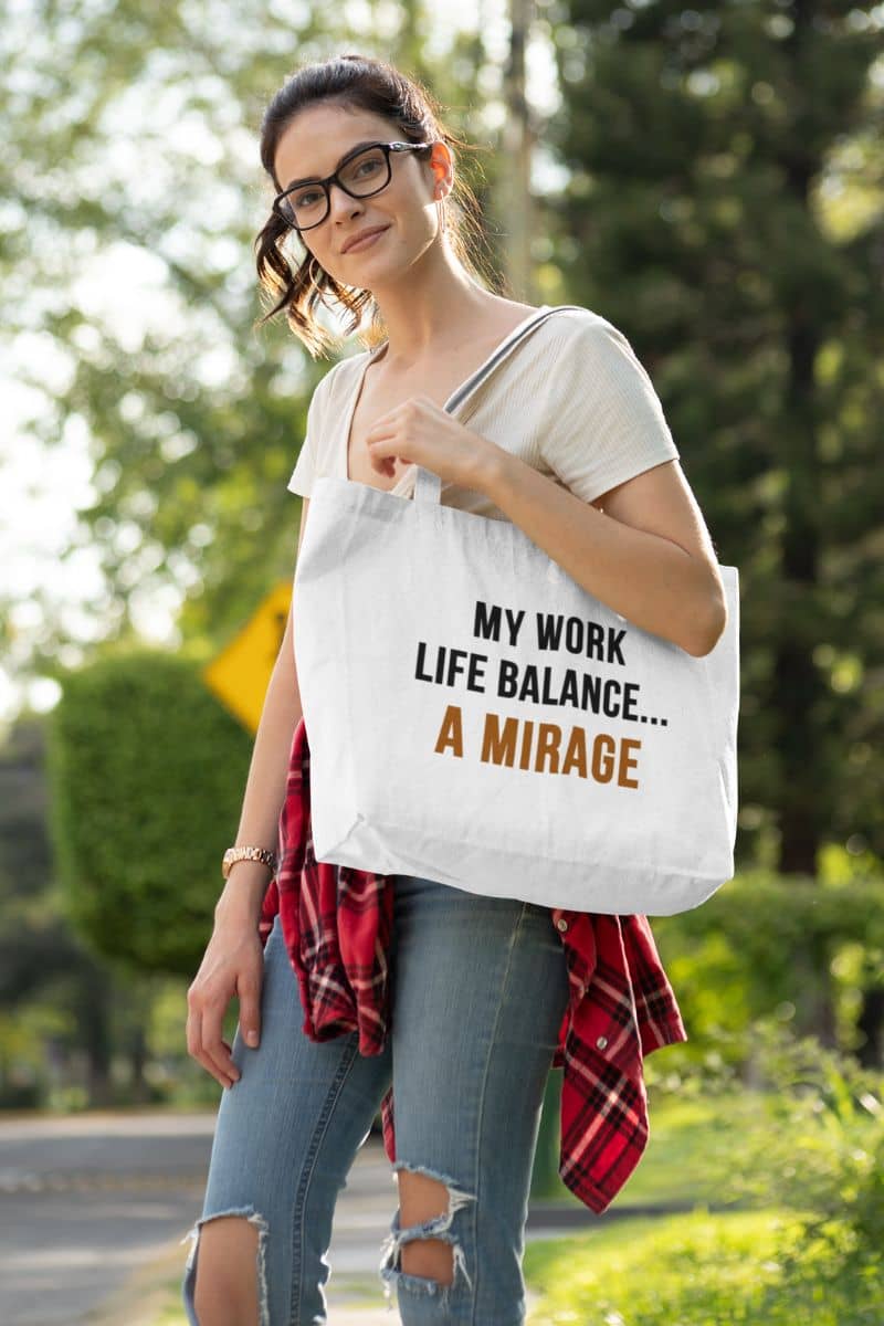 office humor tote bag with a woman holding a tote bag with text 'My Work-Life Balance Is a Mirage' in an outdoor setting