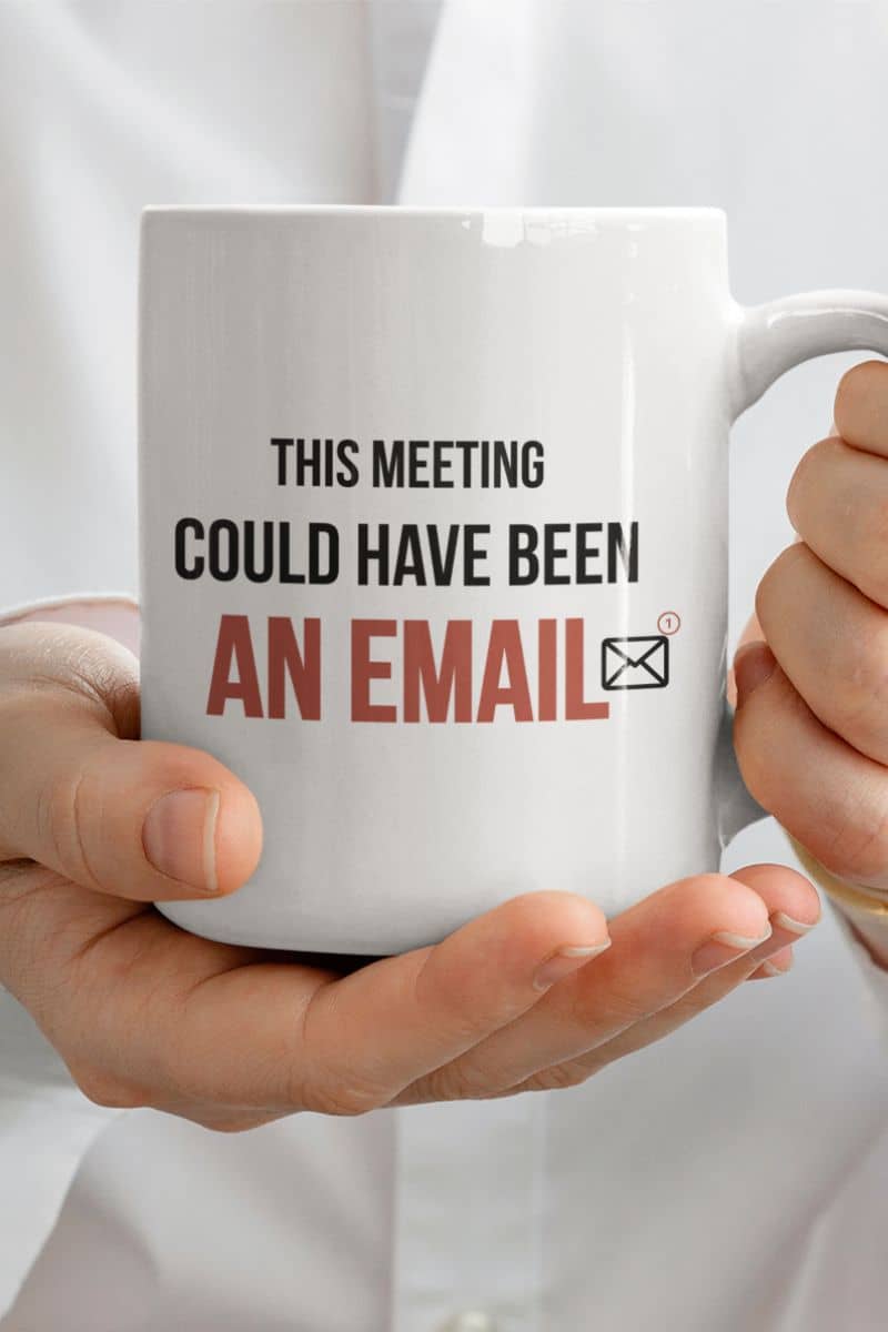 office meeting mug with a person holding a white mug with text 'This meeting could have been an email' on a light background
