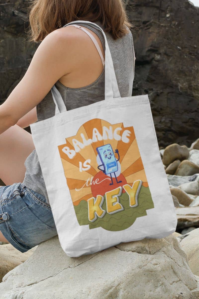 office motivation tote with a person holding a tote bag with 'Balance is the Key' design on a rocky beach.