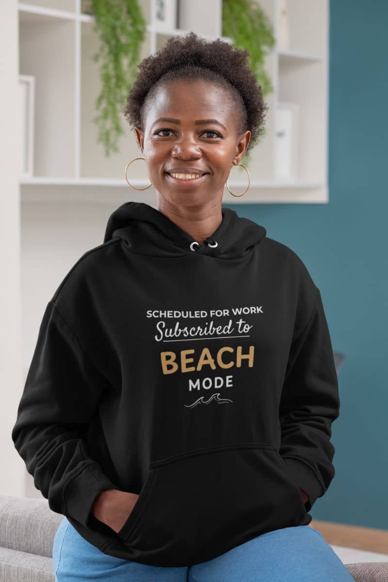 oversized beach sweatshirt with a person wearing a black hoodie with text 'Scheduled for Work. Subscribed to Beach', sitting in a room with shelves and plants.