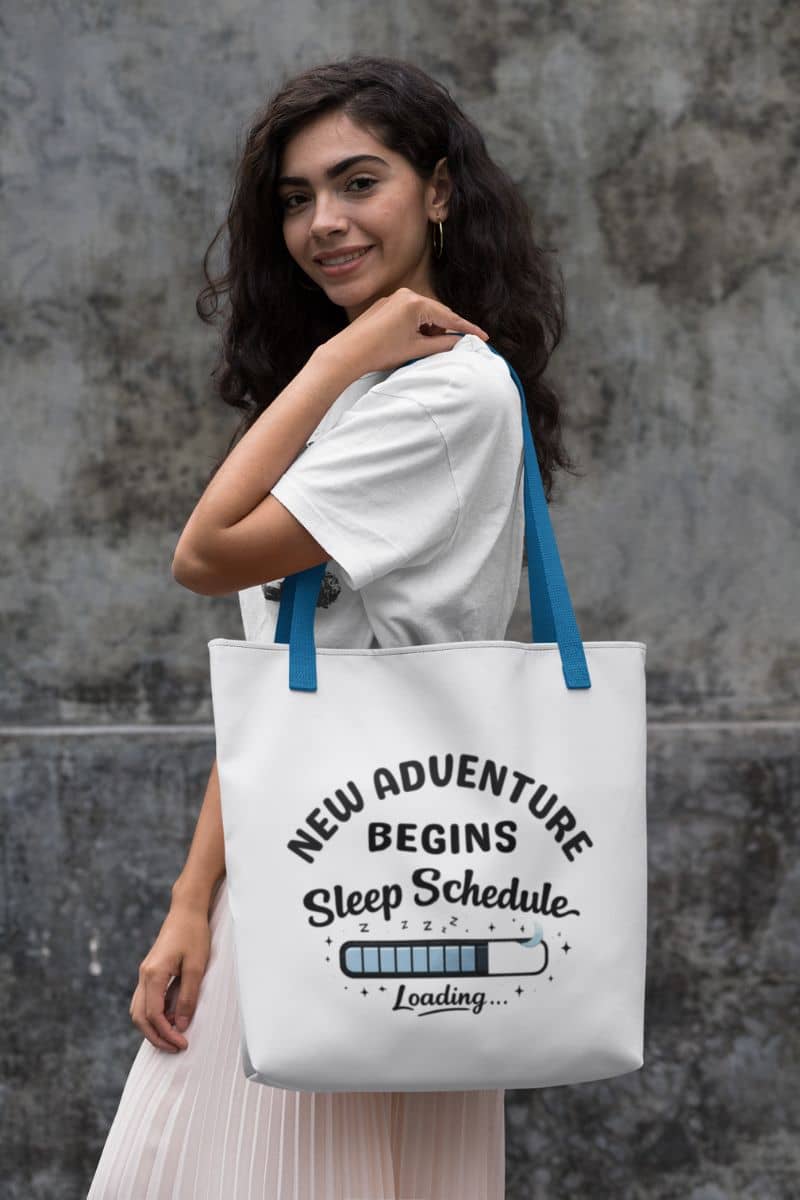 parent life tote bag with a woman holding a tote bag with text 'New Adventure Begins, Sleep Schedule Loading…' against a textured wall.