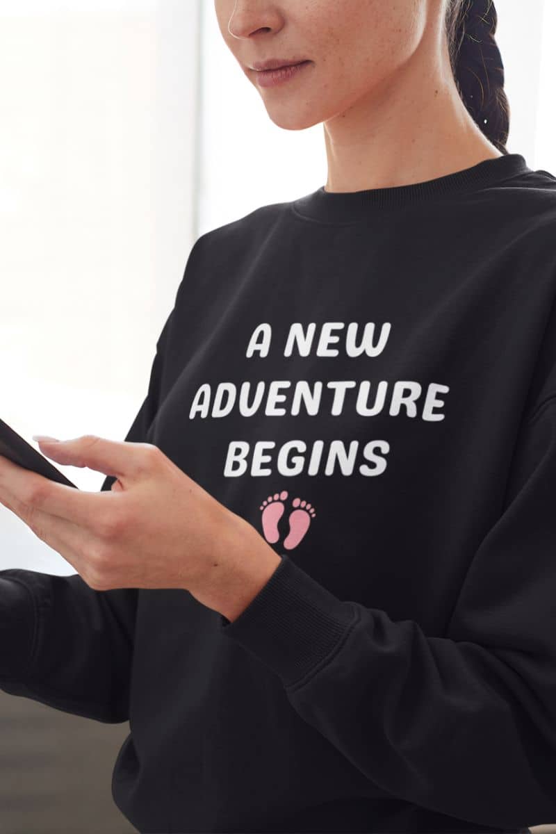 parenthood sweater with a person wearing a black sweatshirt with 'A New Adventure Begins' text and footprints.