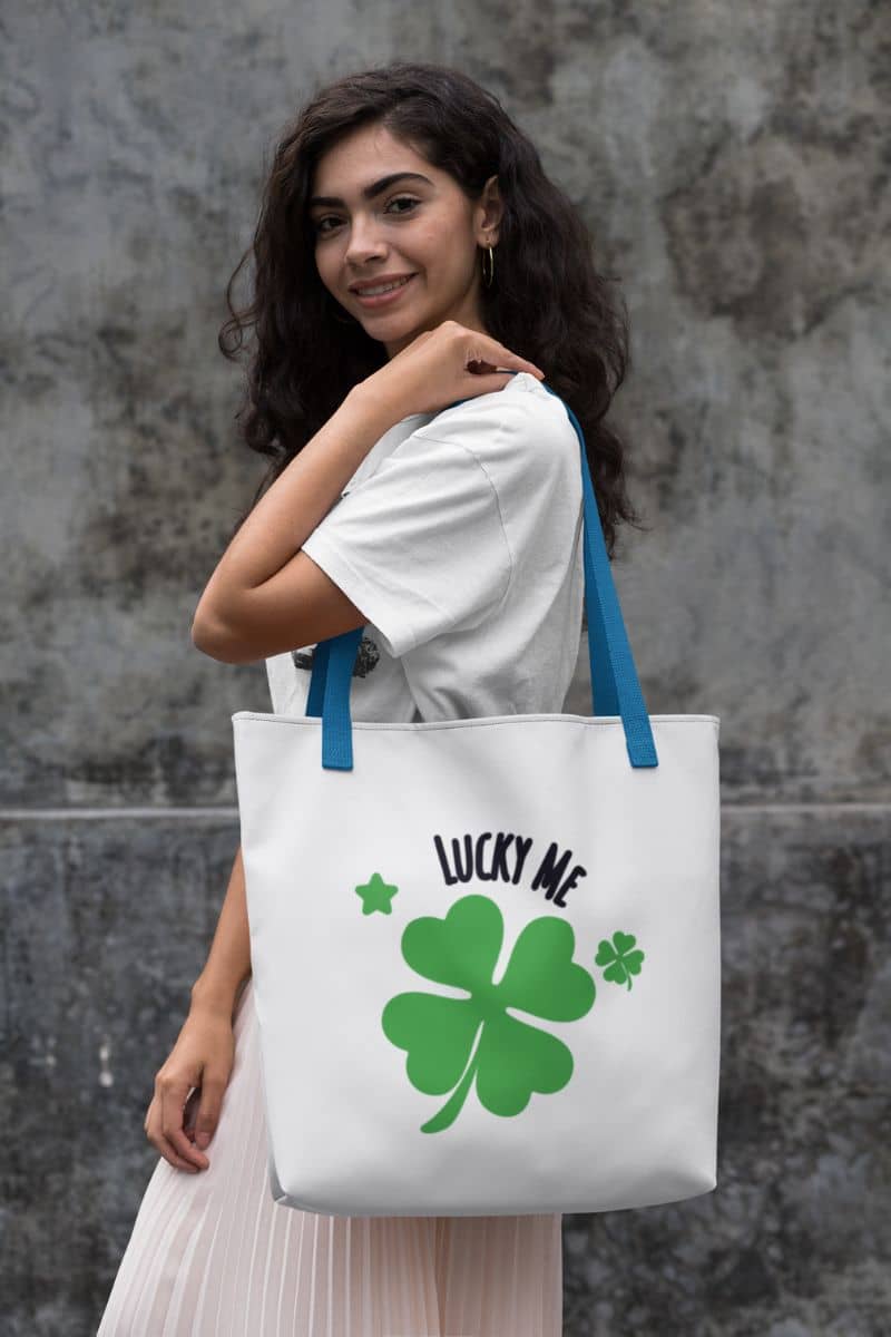positive symbol bag with a woman holding a tote bag with a four-leaf clover design and 'Lucky Me' text against a stone wall.