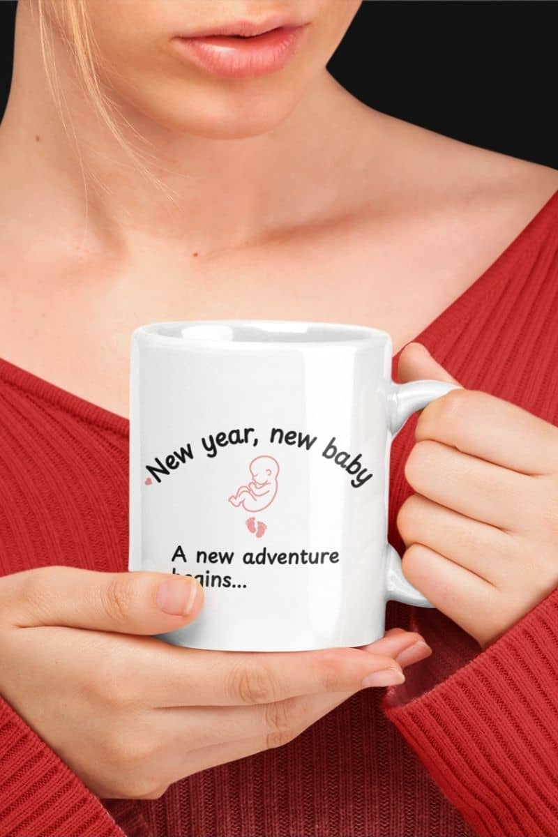 pregnancy announcement coffee mug with a person holding a mug with text 'New year, new baby. A new adventure begins...'