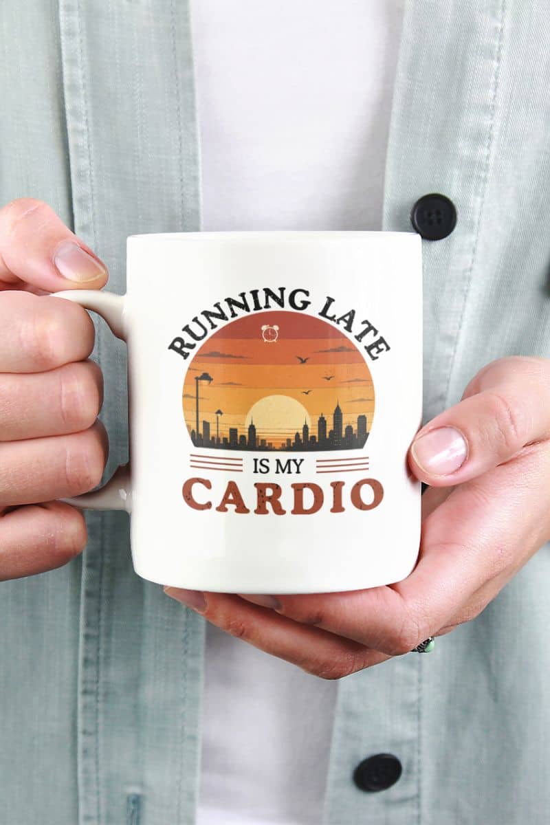 procrastination mug with a person holding a mug with a sunset design and text 'Running late is my cardio' against a light blue shirt background.