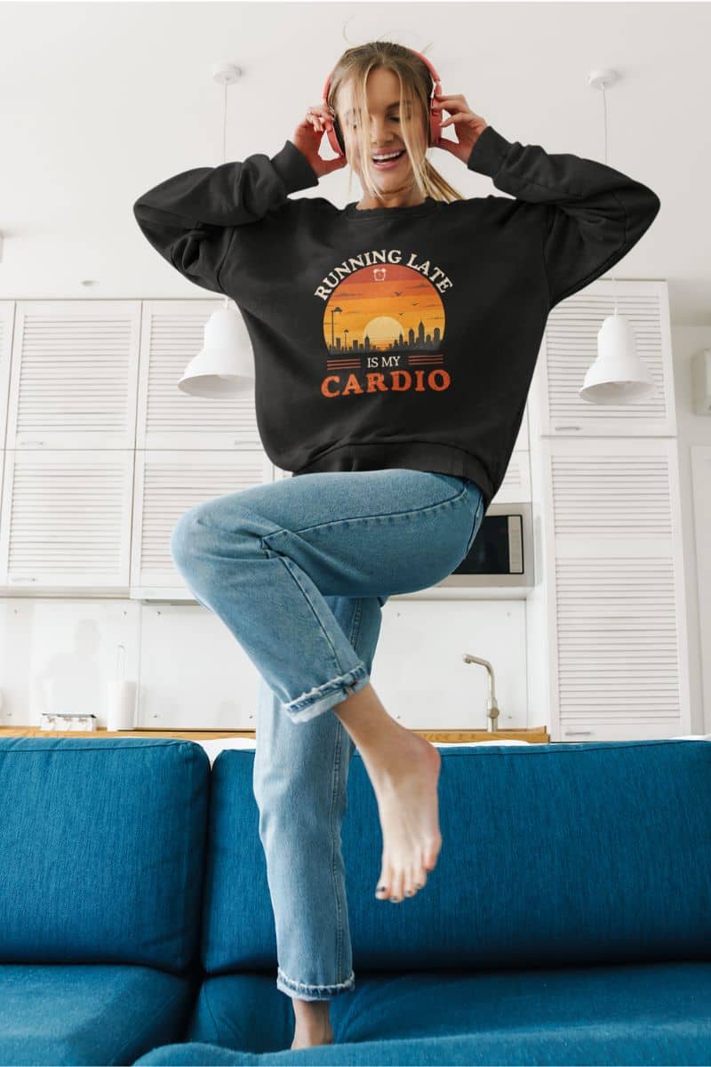 procrastinator sweatshirt with a person wearing a black sweatshirt with a graphic design, standing on a blue couch in a room.