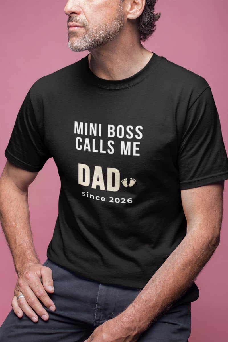 promoted to dad shirt with a man wearing a black t-shirt with text 'Mini Boss Calls Me Dad since 2026' on a pink background