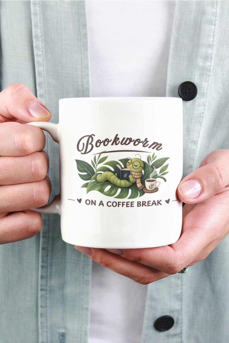 reading mug with a person holding a white ceramic mug featuring the text 'Bookworm ON A COFFEE BREAK'. The person is wearing a light blue button-up shirt over a white undershirt.