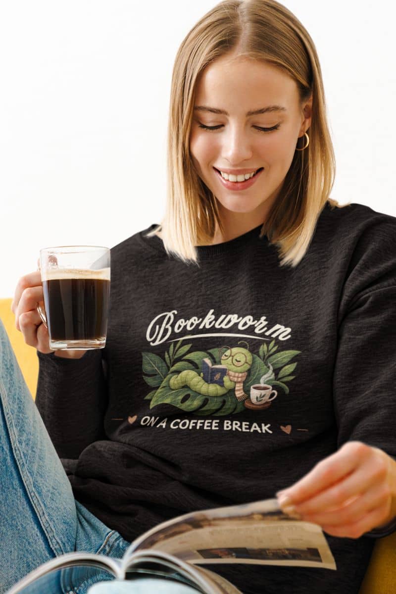 reading sweatshirts with a woman wearing a black sweatshirt featuring the text 'Bookworm ON A COFFEE BREAK', holding a glass of coffee and reading a magazine.
