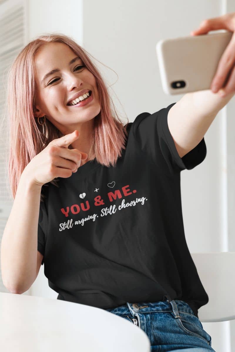 real relationship shirt with a person wearing a black t-shirt with 'YOU & ME. Still arguing. Still choosing.' text, taking a selfie.