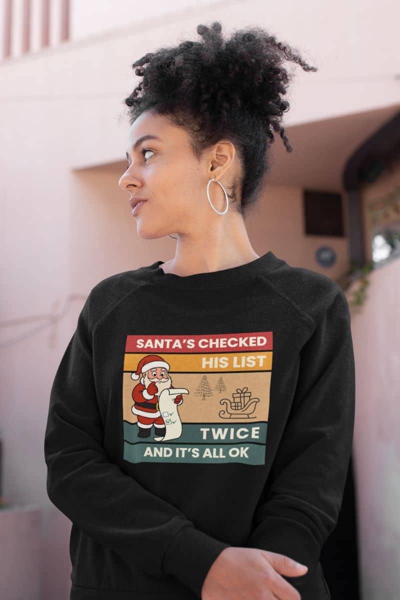 retro santa pullover with a person wearing a black sweatshirt featuring the text 'Santa's Checked His List Twice And It's All Ok'