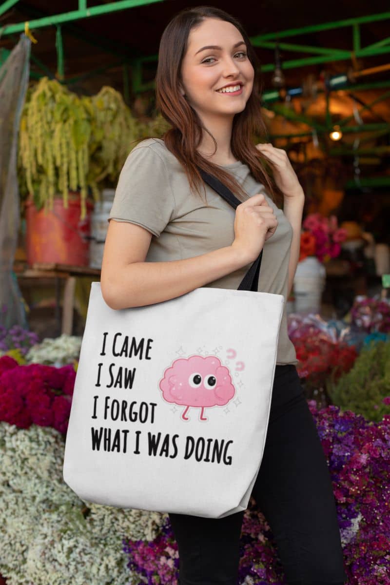 reusable shopping tote with a woman holding a tote bag with text 'I came, I saw, I forgot what I was doing' in an outdoor setting.