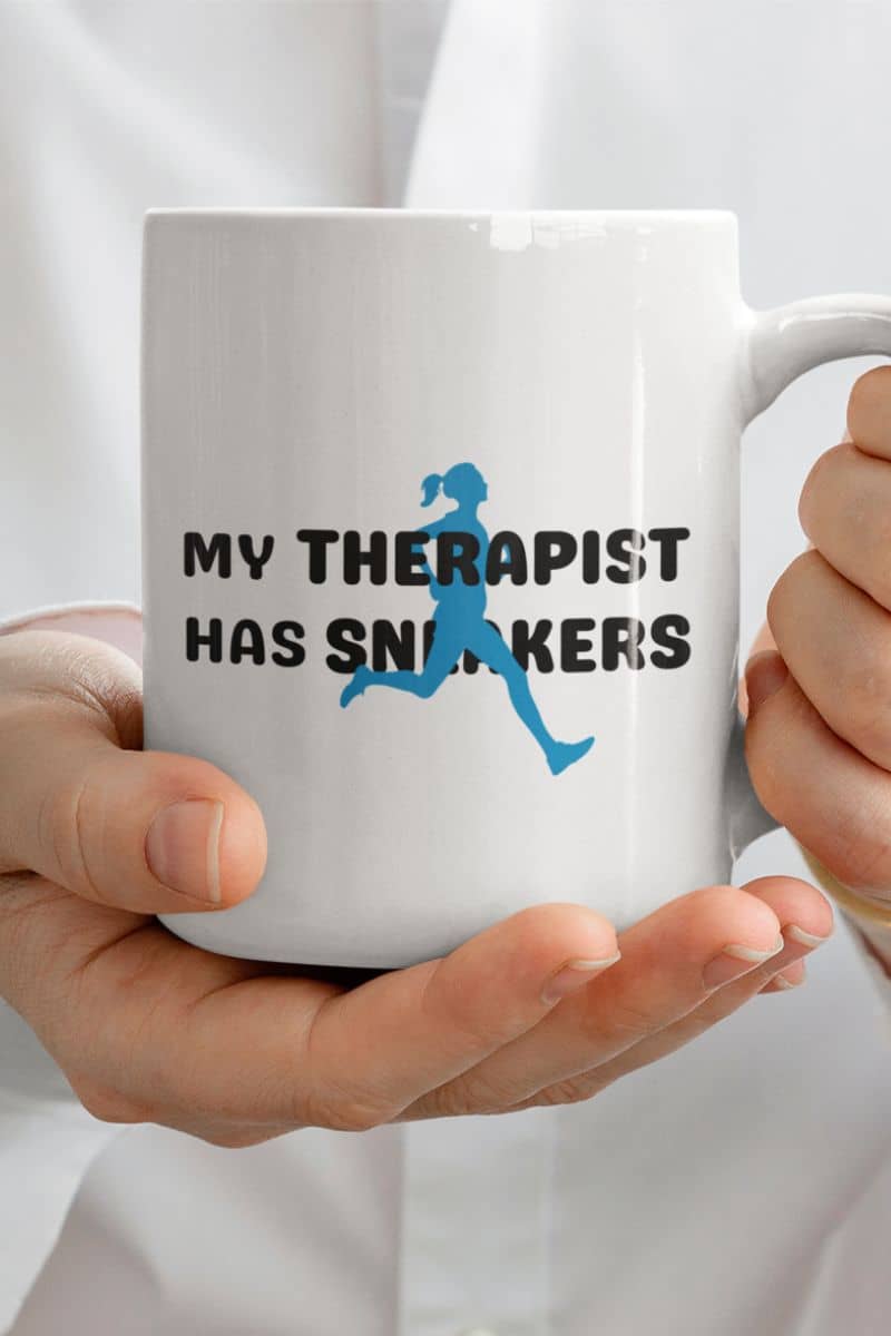 runner gift mug with a white mug with text 'My Therapist Has Sneakers' held by a person against a white background