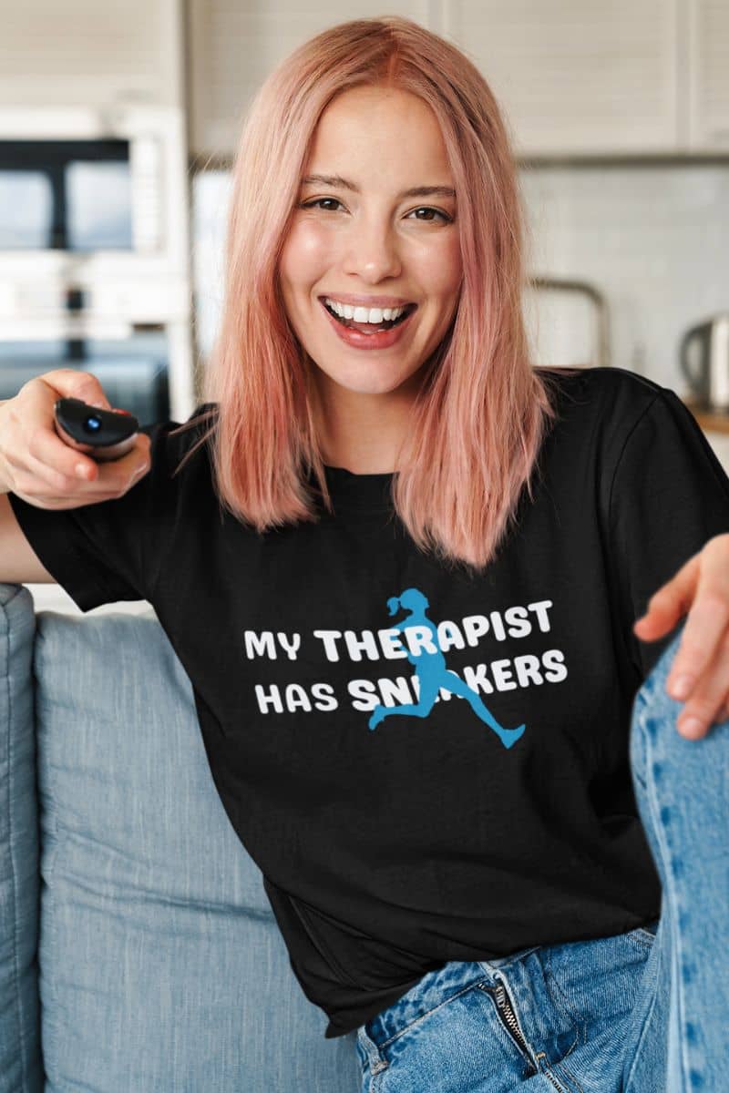 runner gift shirt with a person wearing a black t-shirt with 'My Therapist Has Sneakers' text, sitting on a couch.