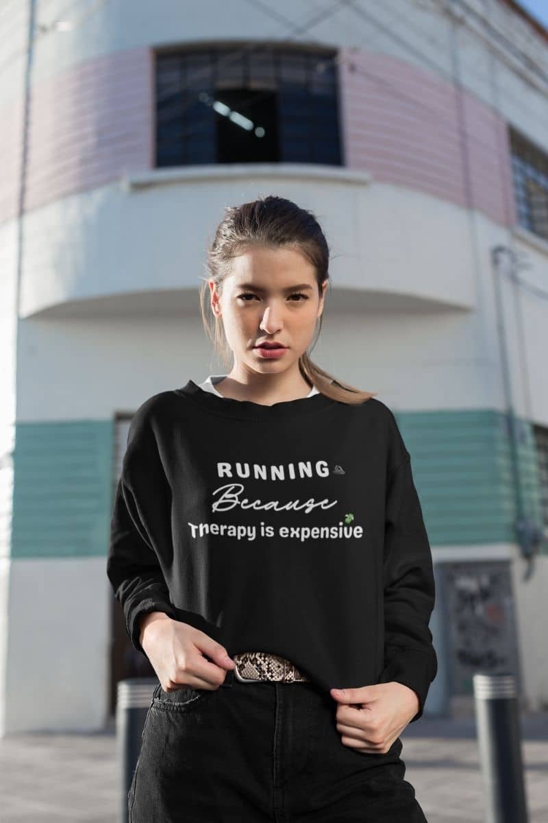 running humor sweatshirt with a woman wearing a black sweatshirt with text 'Running because therapy is expensive', standing in front of a building.