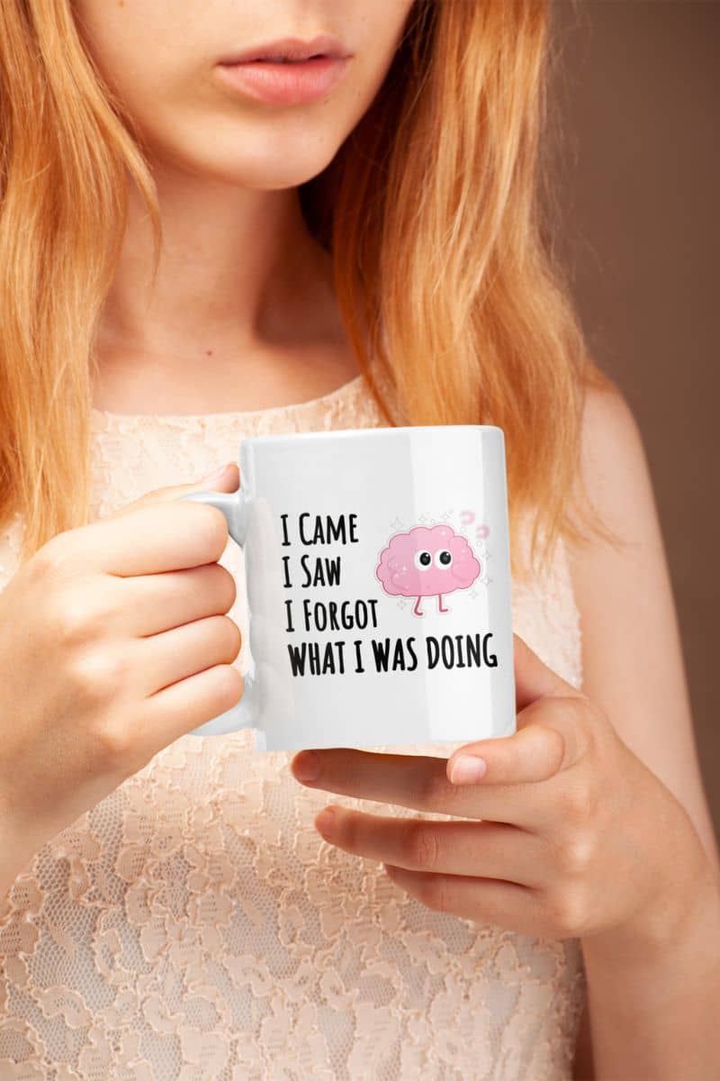 sarcastic ceramic mug with a person holding a mug with humorous text 'I came, I saw, I forgot what I was doing' and a cartoon character.