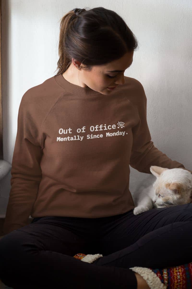 sarcastic cozy sweatshirt with a person wearing a brown sweatshirt with text Out of Office. Mentally Since Monday' sitting next to a cat.