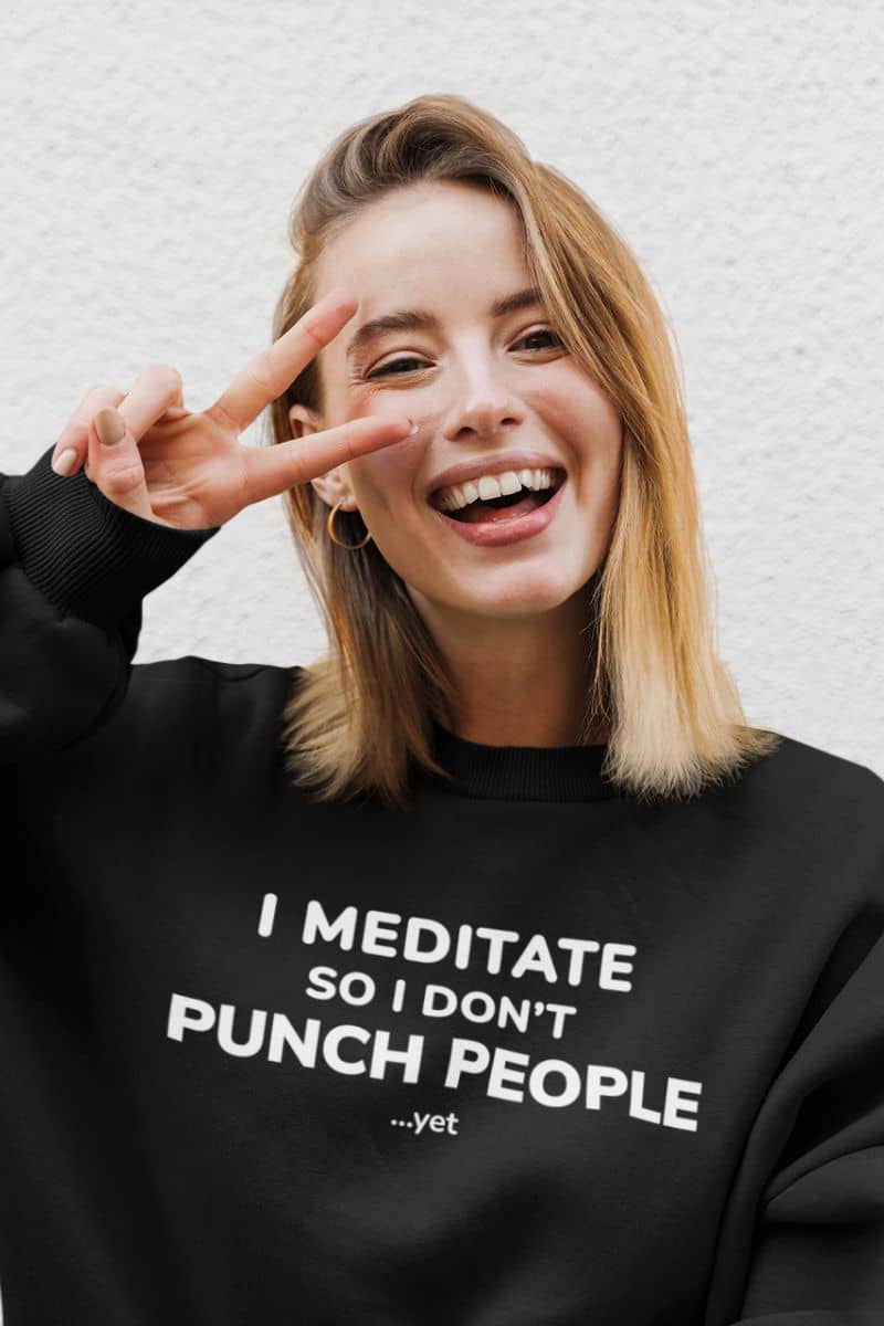 sarcastic humor sweatshirt with a person wearing a black sweatshirt with humorous text 'I Meditate So I Don’t Punch People...yet', making a peace sign.