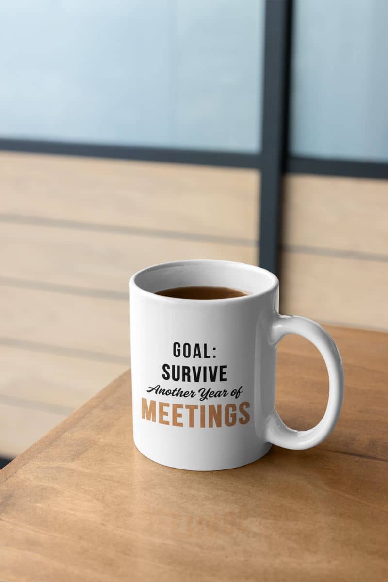 sarcastic office mug with a mug with coffee on a desk, featuring text 'Goal: Survive Another Year of Meetings'.