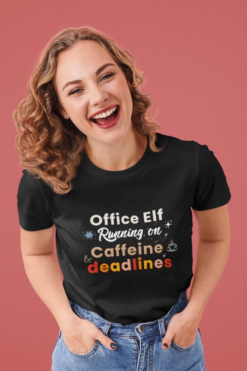 sarcastic office shirt with a woman wearing a black t-shirt with humorous text 'Office Elf, Running on Caffeine & Deadlines' on a pink background