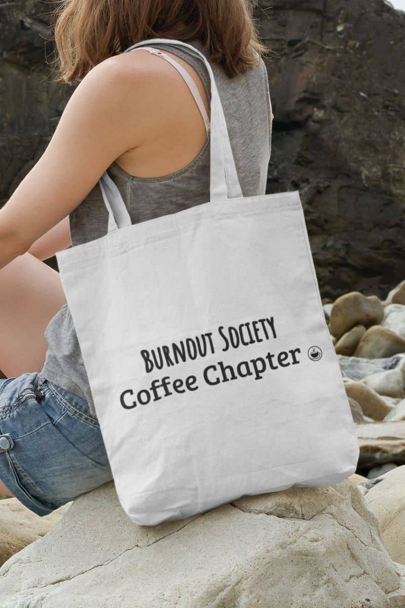 sarcastic work tote with a person sitting on rocks holding a tote bag with 'Burnout Society Coffee Chapter' text.