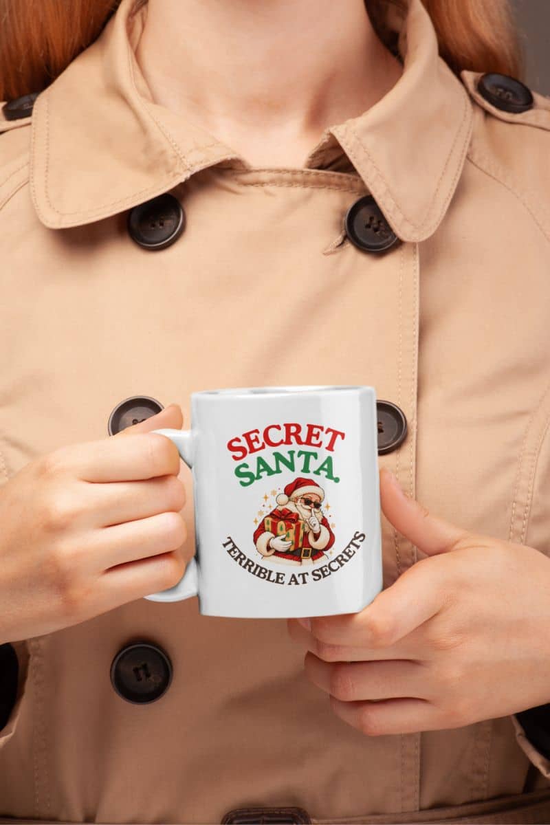 Secret Santa coffee mug with a playful Santa holding a Christmas gift, held by a woman wearing a beige coat.