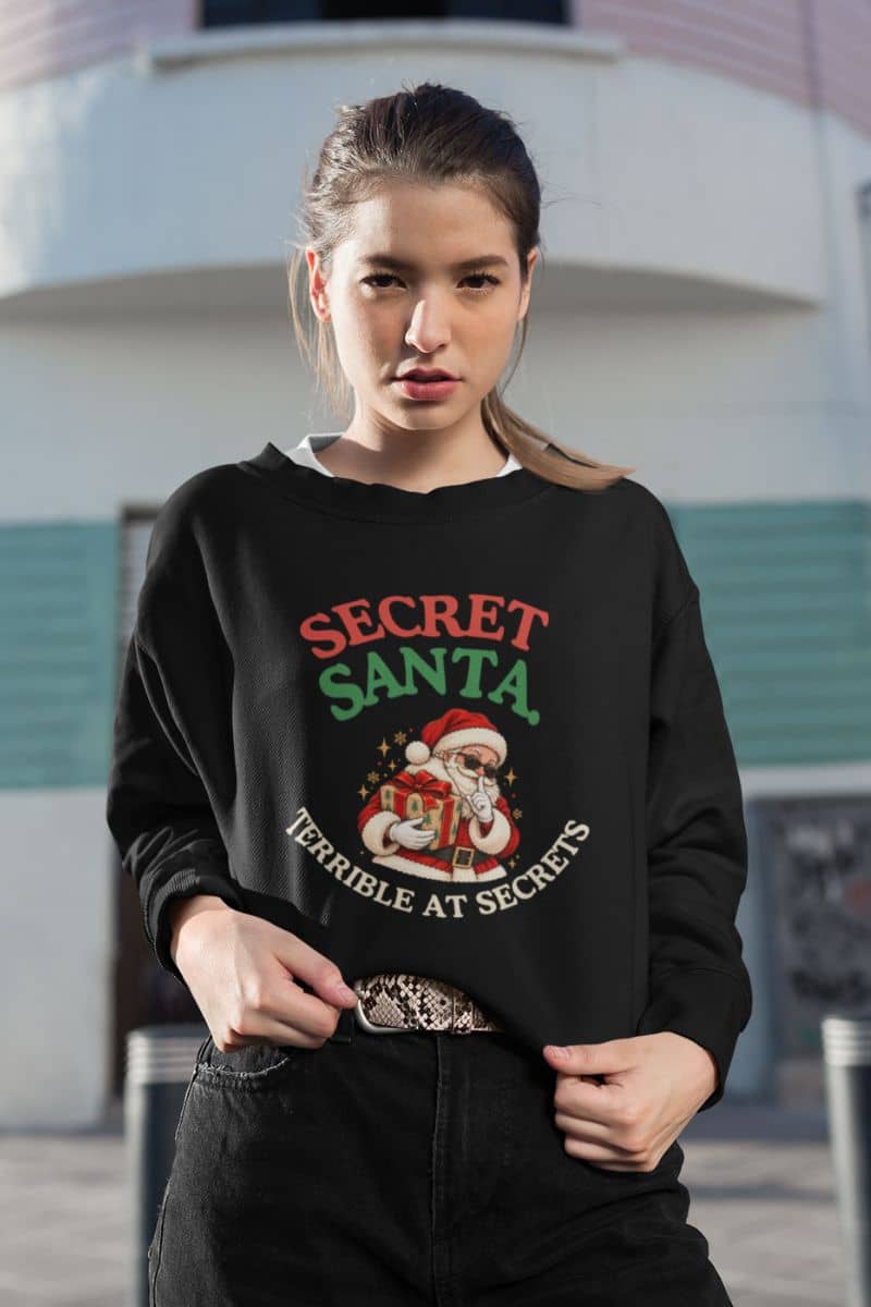 Secret Santa sweatshirt featuring the Terrible at Secrets Christmas design on a black crewneck styled with dark jeans.