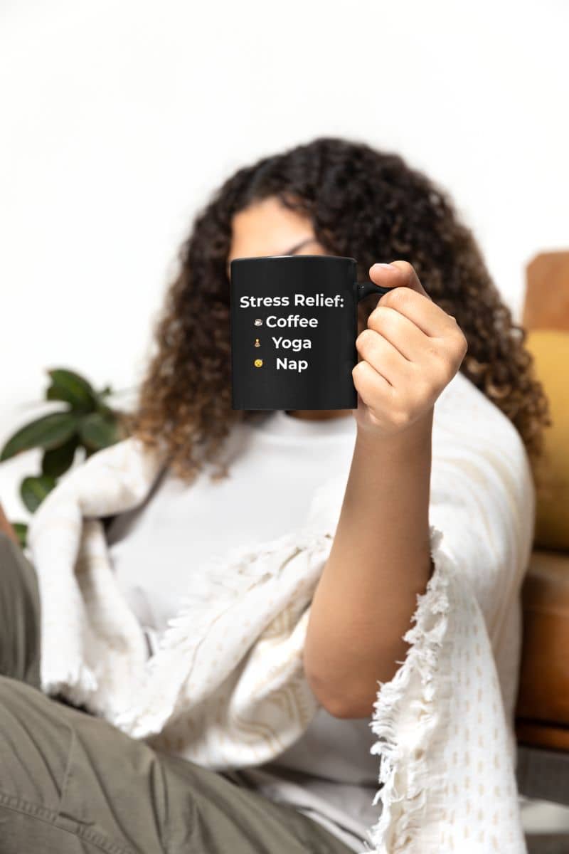 self-care coffee mug with a person holding a mug with 'Stress Relief: Coffee Yoga Nap' text, sitting on a couch.