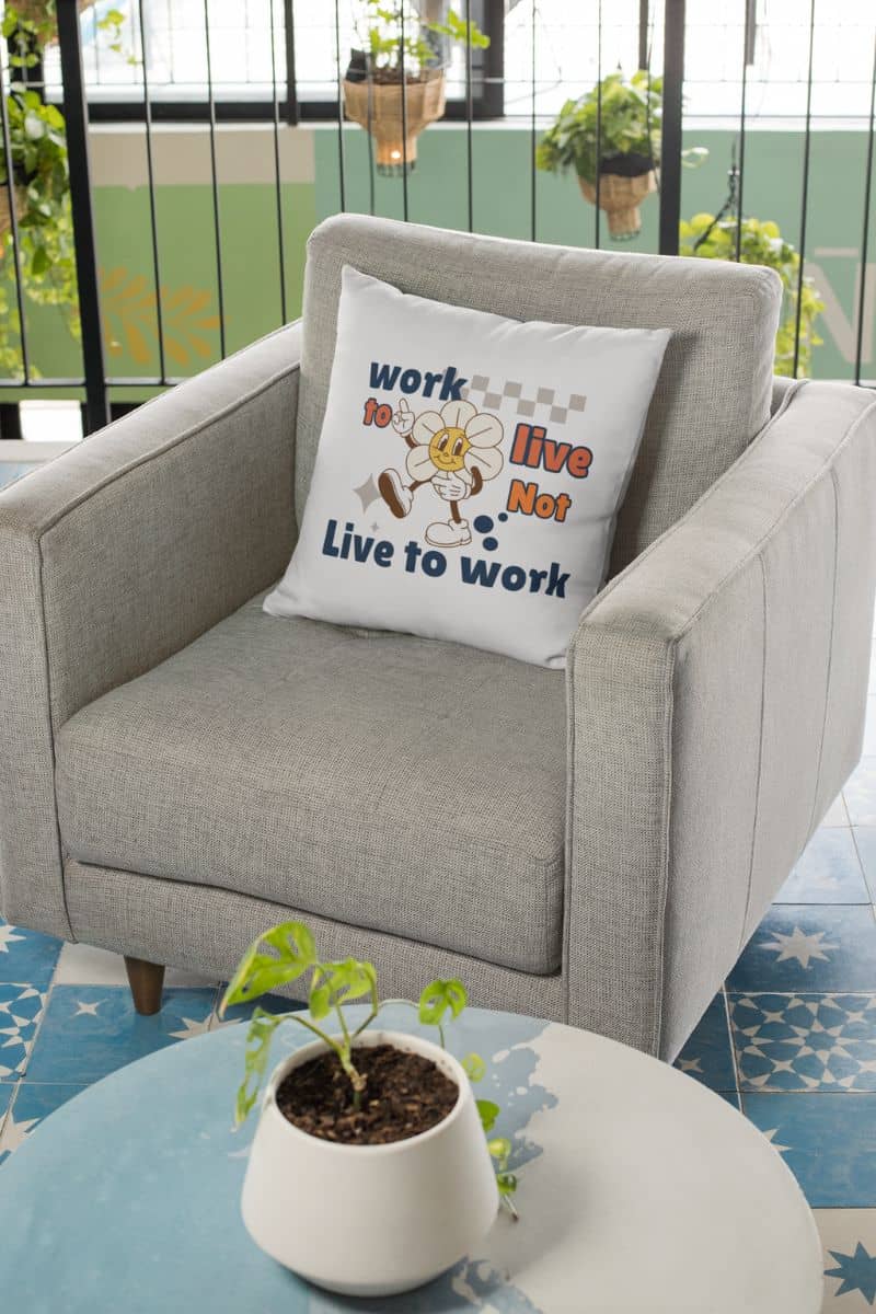 self care decorative pillow with a gray armchair with a pillow featuring motivational text 'Work to Live, Not Live to Work', placed on a balcony with plants and a blue floor.