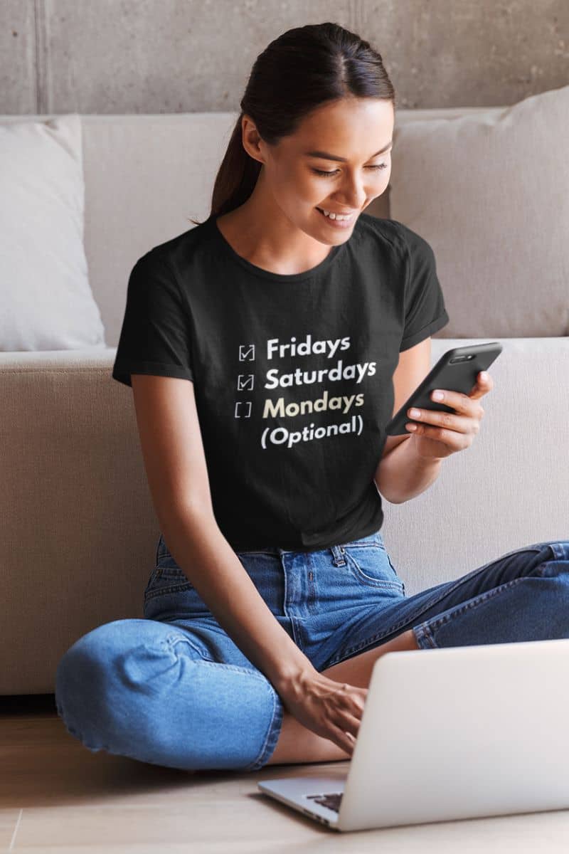 simple funny t-shirt with a woman sitting on a couch using a phone with a black t-shirt featuring text 'Fridays and Saturdays, Mondays (Optional)'.