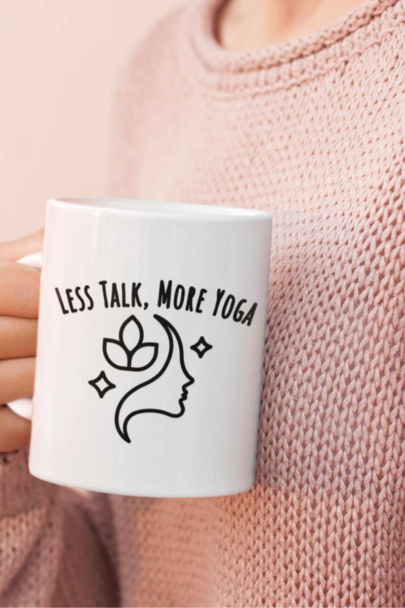 slow morning routine mug with a white mug with 'Less Talk, More Yoga' text and face design held by a person wearing a pink sweater.