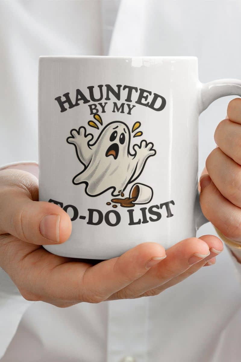 A spooky mug featuring a “Haunted by My To-Do List” funny ghost, shown on a white ceramic mug held by a person.