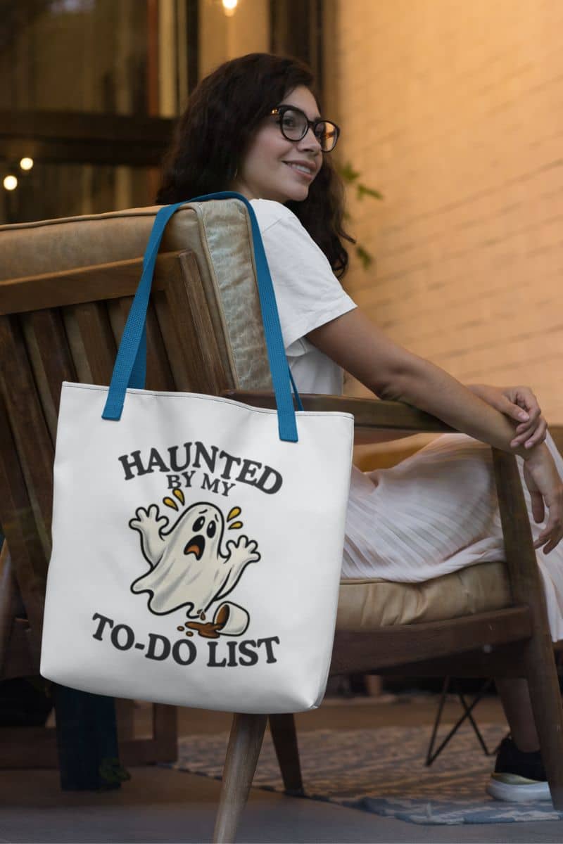 A spooky tote featuring a “Haunted by My To-Do List” funny ghost, hanging on the chair in a coffee shop