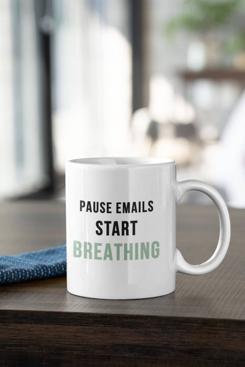 stress relief coffee mug with a white mug with text 'Pause Emails, Start Breathing' on a wooden surface.
