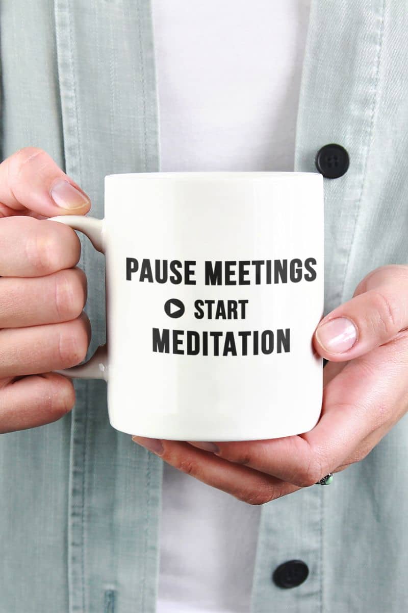 stress relief mug with a person holding a mug featuring the text 'Pause Meetings, Start Meditation'