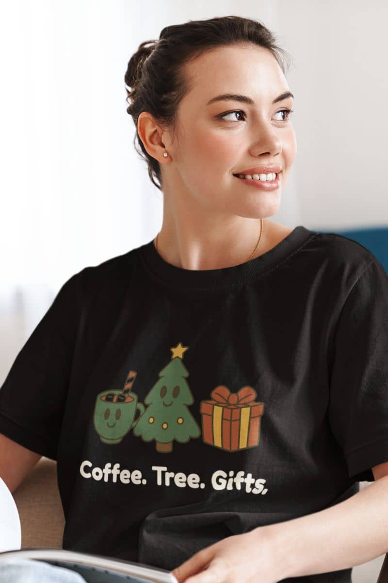 subtle christmas tee with a woman wearing a black t-shirt with Christmas-themed graphics and text 'Coffee. Tree. Gifts.'.