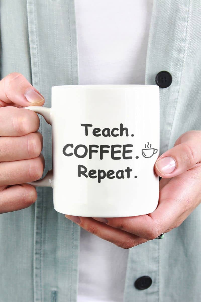 teacher appreciation gift with a person holding a white ceramic coffee mug with text 'Teach. Coffee. Repeat.'