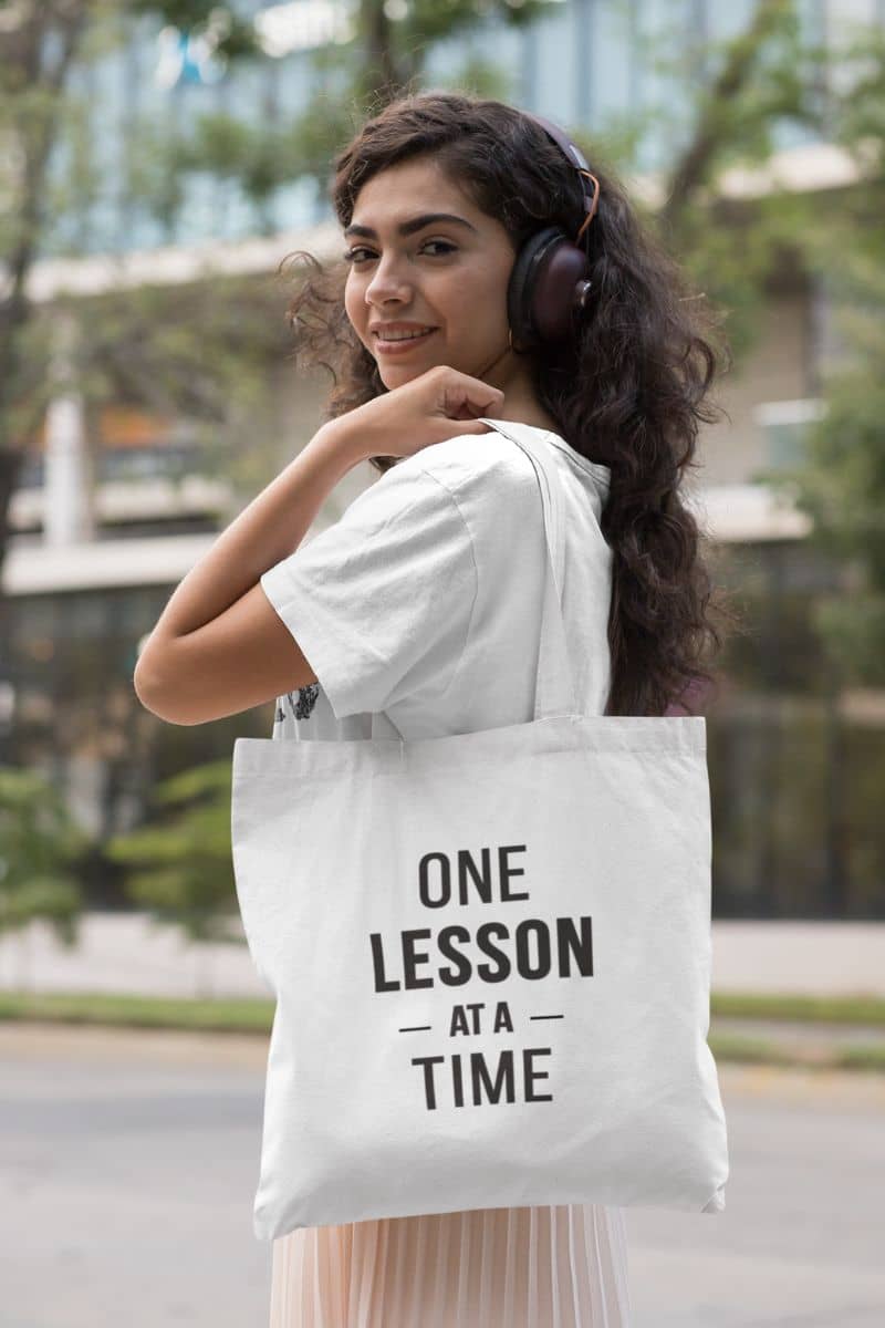 teacher carry bag with a woman carrying a white tote bag featuring the text 'ONE LESSON AT A TIME'