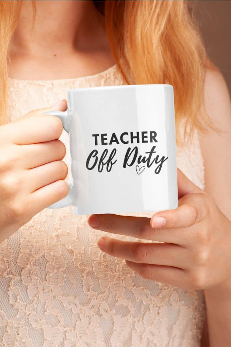 teacher ceramic mug with a person holding a white ceramic mug featuring the text 'TEACHER Off Duty' printed in black, wearing a light beige lace top.