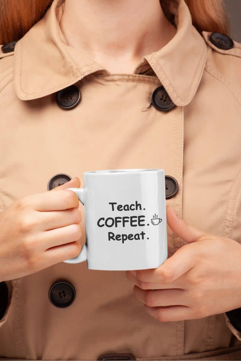 teacher coffee mug with a person in a beige trench coat holds a white mug with text 'Teach. Coffee. Repeat.'