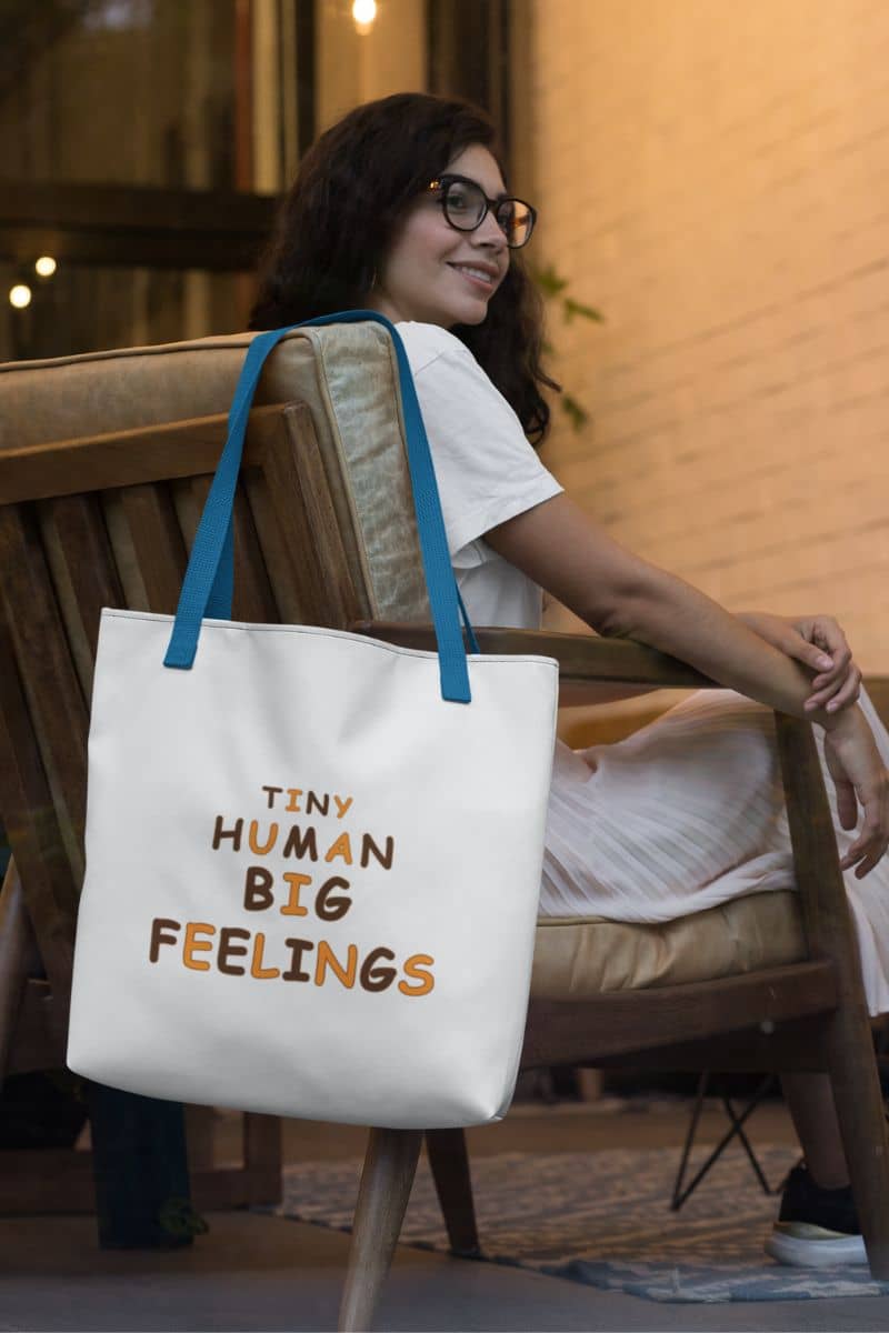 teacher gift bag featuring a large white tote bag with text 'TINY HUMAN BIG FEELINGS', hanging on the chair.