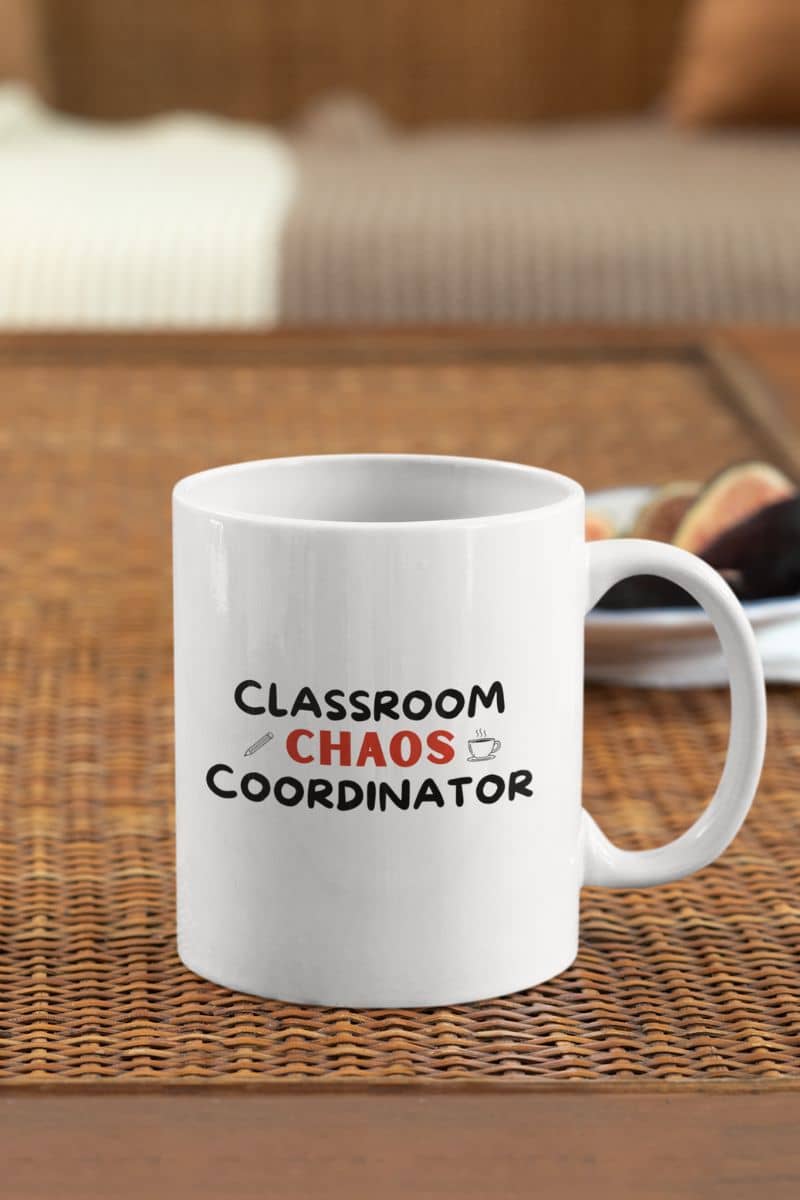 teacher gift mug with a white ceramic coffee mug with the text 'Classroom Chaos Coordinator' printed on it, resting on a brown woven placemat with a blurred indoor background.