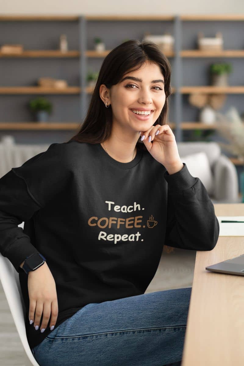 teacher sweater with a woman wearing a black sweatshirt featuring the text 'Teach. Coffee. Repeat.'