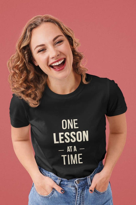 teacher tee with a woman wearing a black t-shirt featuring the text 'ONE LESSON AT A TIME' against on a red background.