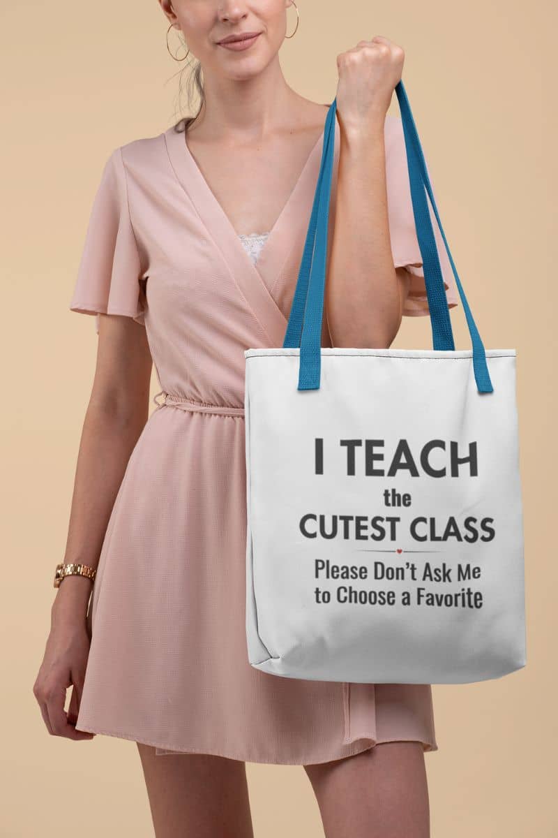teacher tote bag held by a woman, featuring the bag with text that reads, 'I Teach the Cutest Class. Please Don’t Ask Me to Choose a Favorite'.