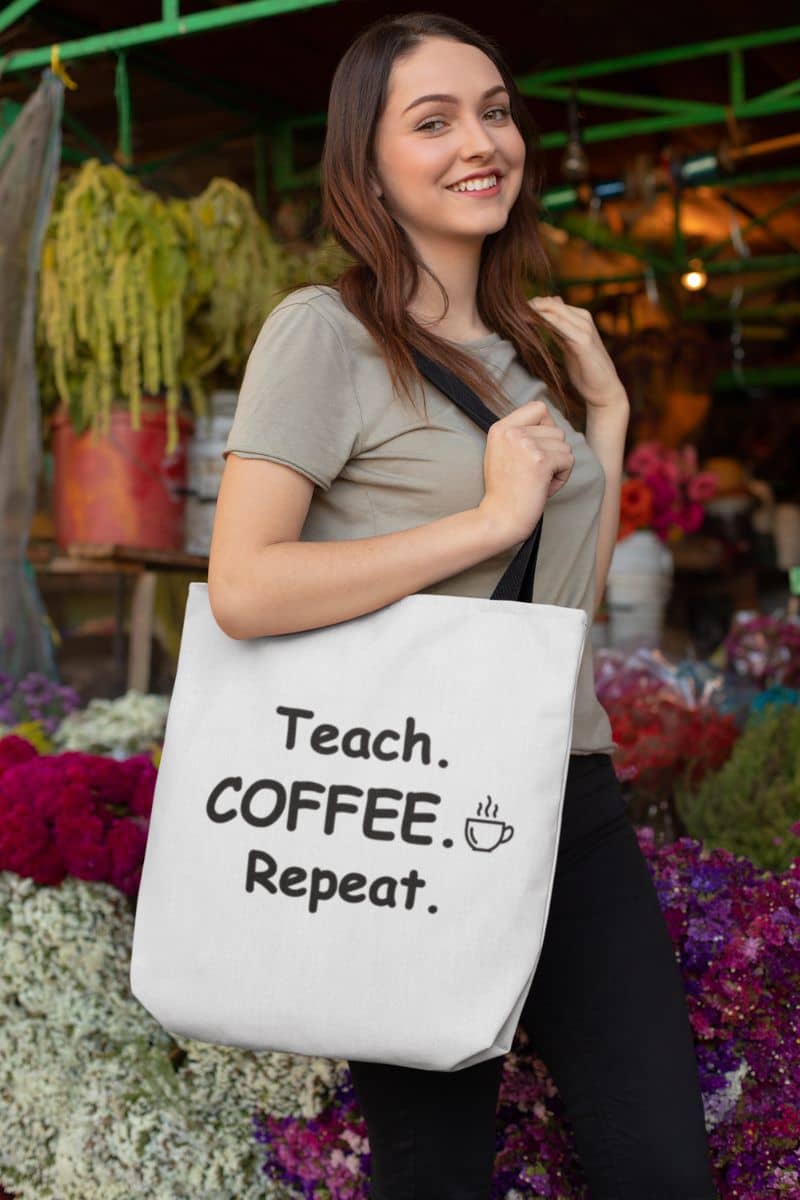 teacher tote bag with a woman holding a tote bag with text 'Teach. Coffee. Repeat.' in a market setting
