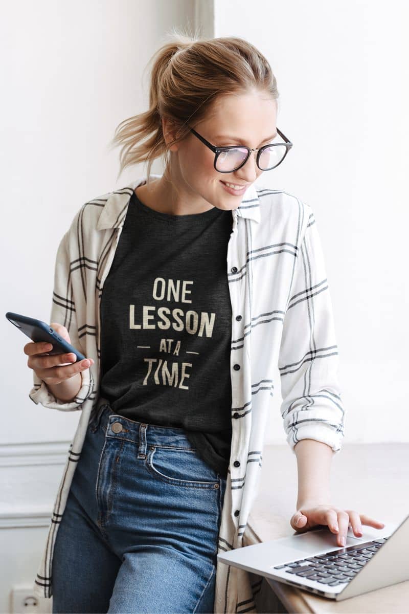 teaching t shirt with a woman wearing a black t-shirt that reads 'ONE LESSON AT A TIME' .