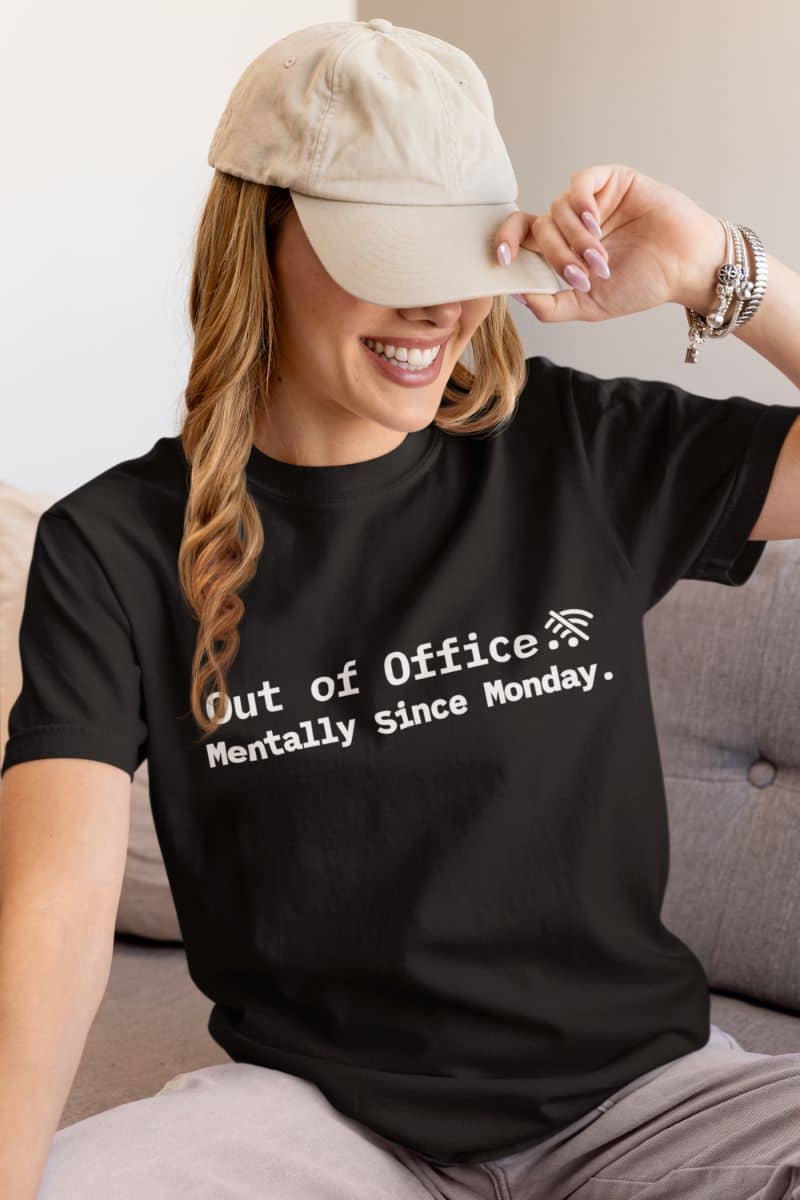 tired but trying tee with a person wearing a black t-shirt with 'Out of Office Mentally since Monday' text, sitting on a couch.